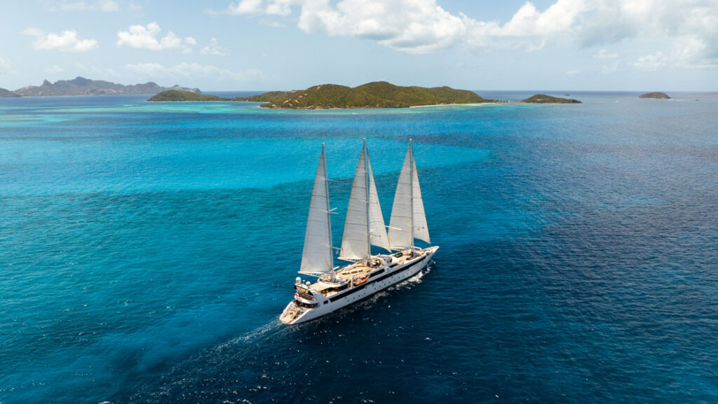 Aerial view of Le Ponant white sailing ship with 3 masts cruising through turquoise sea on a sunny day in the Caribbean.