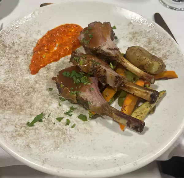 Lambchops on bone sit beside smear or red sauce & roasted vegetables on a white plate, served on Galileo cruise ship in Greece.