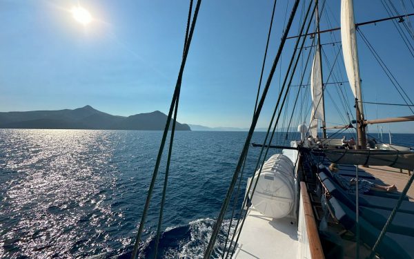 Galileo cruise ship sailing out at sea on a sunny day in Greece with woman on blue padded chaise lounger under rigging & sails.