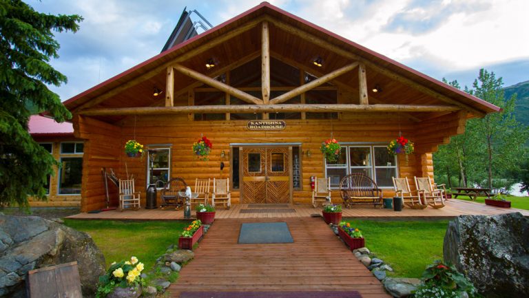 Exterior shot of Kantishna Roadhouse Lodge in Alaska with log cabin construction, potted flowers by walkway & green lawn.