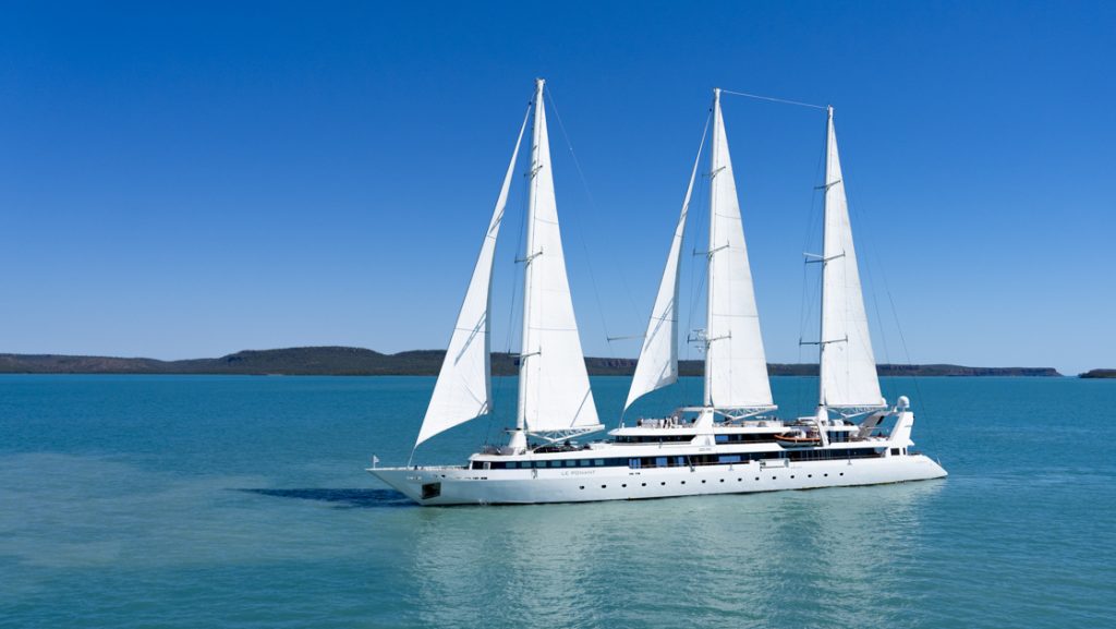 Exterior of Le Ponant white small sailing ship with 3 masts & 5 sails cruising in calm turquoise water on a sunny day.