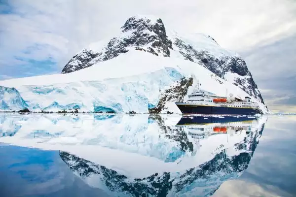 With water like glass the snow covered Antarctica landscape and National Geographic small ship have a perfect mirrored reflection
