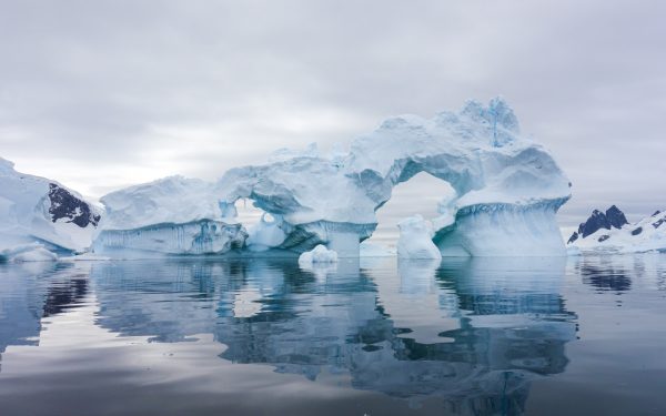 showcasing the antarctica climate with overcast skies and a large iceberg with a hole in it in the foreground