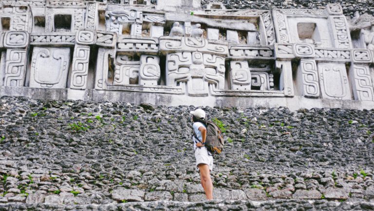 Woman on a Belize jungle tour via Chaa Creek stands on stone steps & looks up at white Aztec stone carvings.