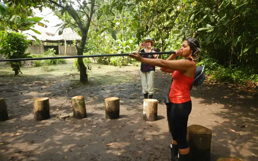 woman in a red shirt holding a blowgun to her mouth on an Ecuador amazon land tour