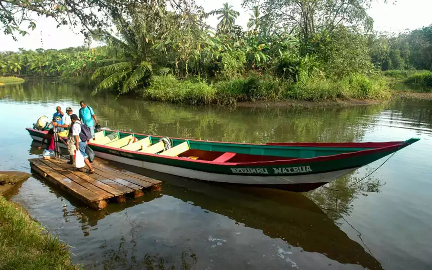 a large dugout canoe is tied to a small pier on a river while adventure travelers step out of it to start the best of panama land tour