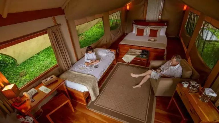 2 guests enjoying their safari tent that has 2 beds and places to hangout, a modern yet traditional safari look
