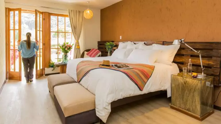 women peering off through the window in her guestroom with a large king bed and white sheets