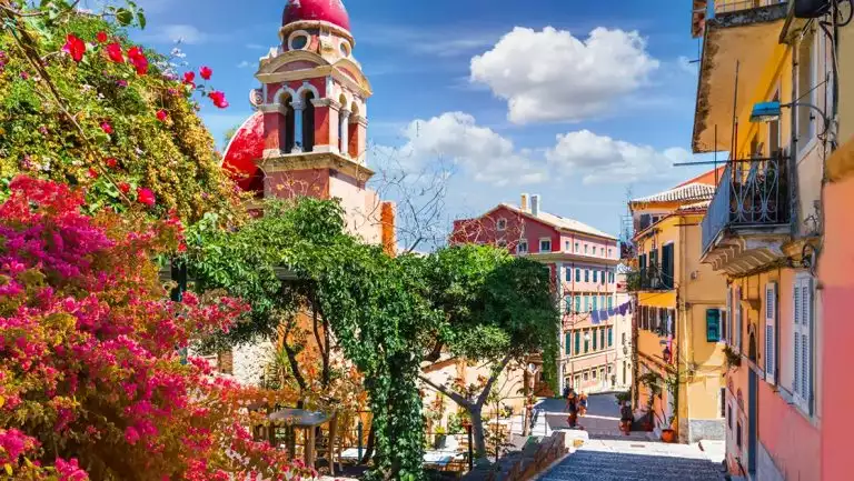 Greek street with colorful buildings and bright blooming greenery around the cobblestone path.