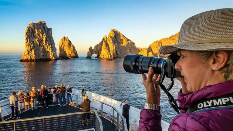 Guests gather on the bow of the ship National Geographic Venture and photograph the sunrise at Lands End, Cabo San Lucas, Baja California, Mexico