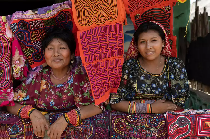 2 women sit & smile among brightly colored, woven textiles, seen on a Panama & Colombia small ship cruise.