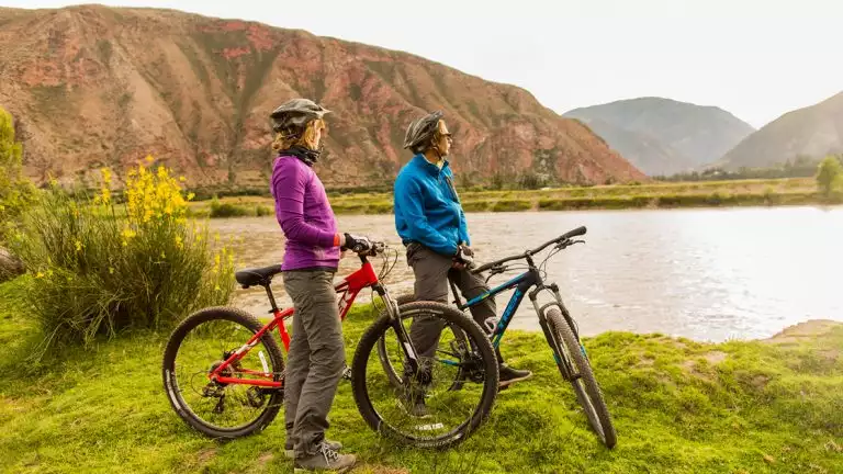 Couple on mountain bikes looking out into the distance overlooking a small lake on a warm sunny day next ti the mounatins