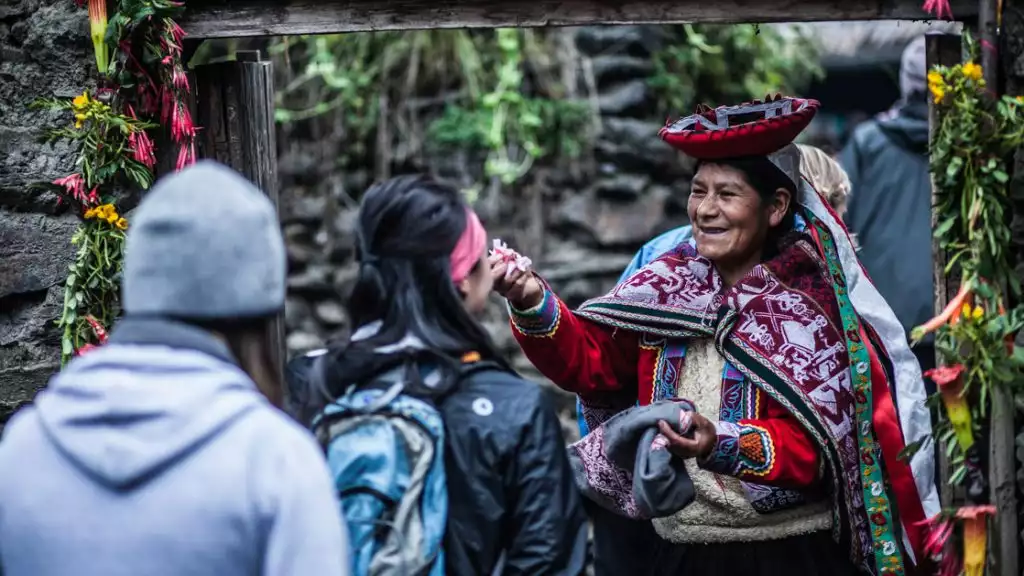 Women in tradtional peru outfit greeting travelers as they enter the scared valley next to the stone walls and flowers all around