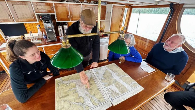 Captain bill and guests gather around table aboard westward yacht and look at map of inside passage Alaska to plan their route