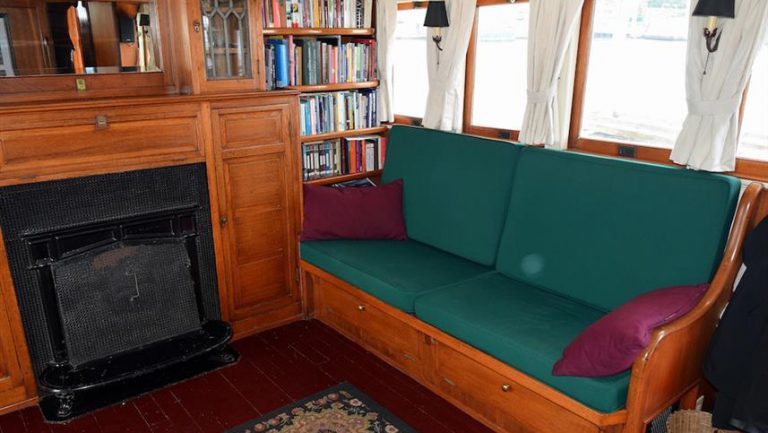 interior living room area aboard historic yacht westward green and wooden couch in front of black iron fireplace