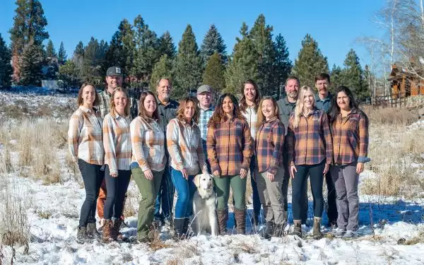 AdventureSmith Explorations staff members pose in two rows wearing plaid long sleeve shirts on a winter blue bird day