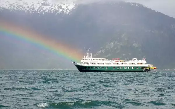 A rainbow seen with one end touching the bow of a white small ship with a green hull in Alaska