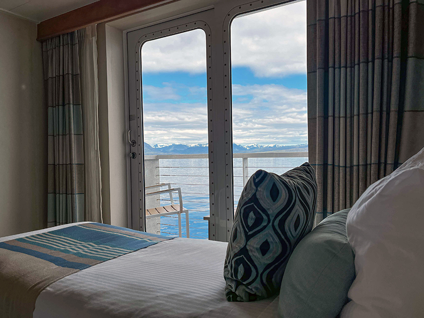 A luxury cabin with in Alaska seen from the bedside looking out over the bed to the balcony and snow-covered mountains
