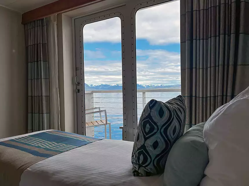 A luxury cabin with in Alaska seen from the bedside looking out over the bed to the balcony and snow-covered mountains