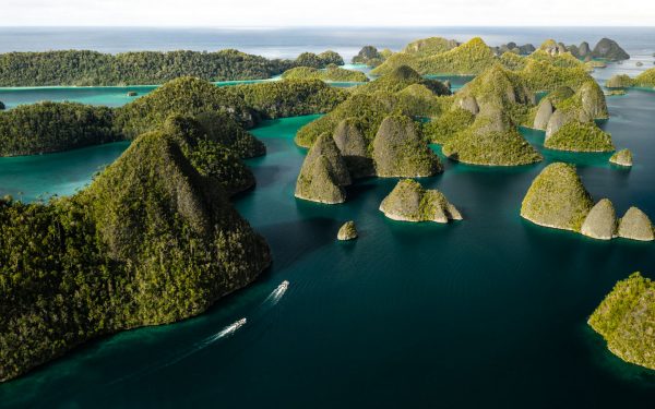 Aerial view of karst gum drop islands in turquoise sea with 2 small Zodiac boats cruising under bright skies in Indonesia.