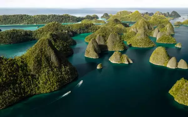 Aerial view of karst gum drop islands in turquoise sea with 2 small Zodiac boats cruising under bright skies in Indonesia.