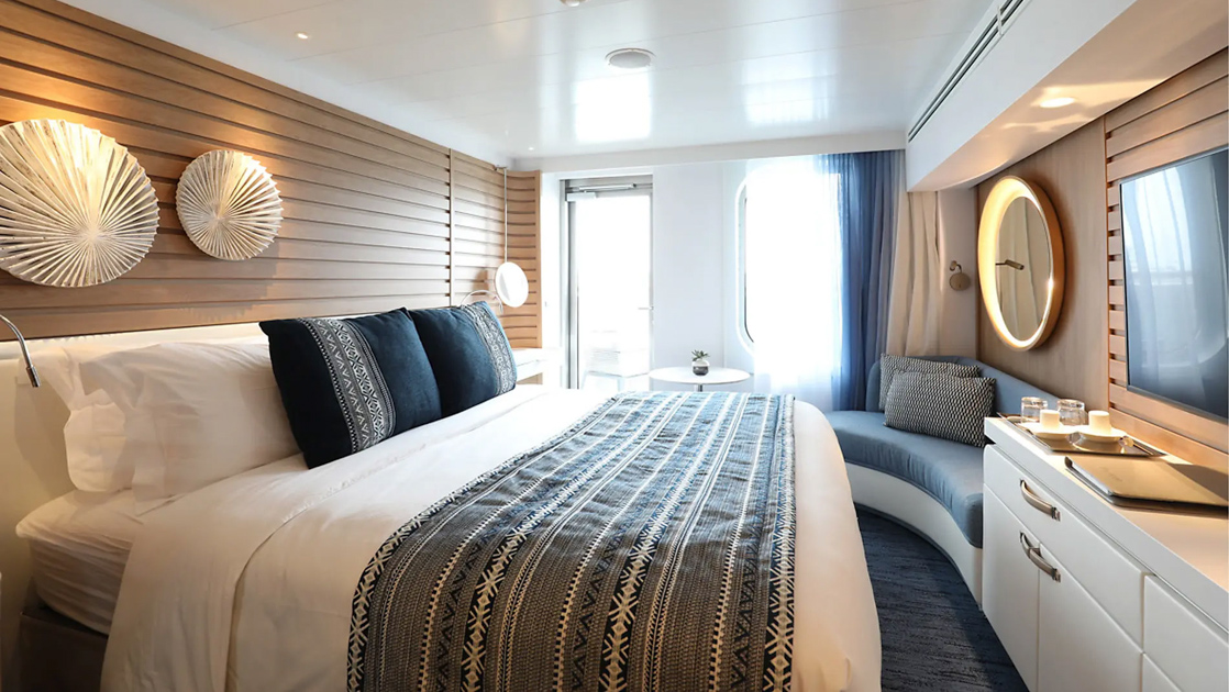 Deluxe Stateroom on Le Laperouse French ship, with king bed, white dresser, private balcony, sofa & ethic-yet-chic decor.