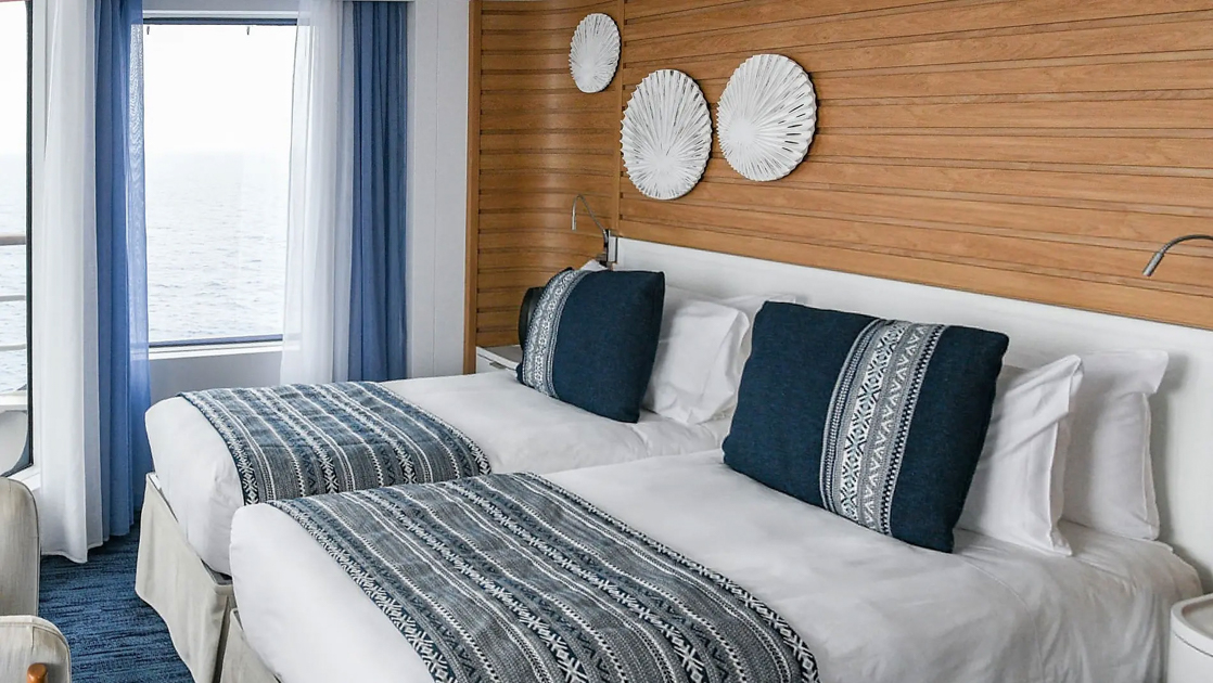 Grand Deluxe Suite on French ship Le Laperouse, with ethnic chic decor, wood walls, twin beds & separate living room.