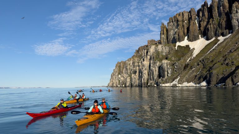 Red and yellow kayaks in the calm seas off the steep snowy cliffs