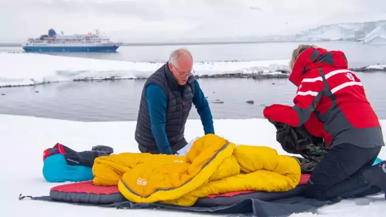 Antarctic campers roll up their gear from the night prior on the snow and ice next to the the water where their small cruise ship is parked