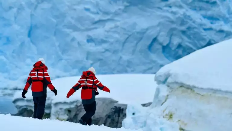 Hikers in winter gear and red adventure jackets walk down as they navigate the glaciers and snow