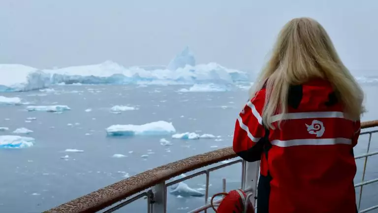 Women looks off into the distance off small cruise ship into icy landscape and broken up iceberg