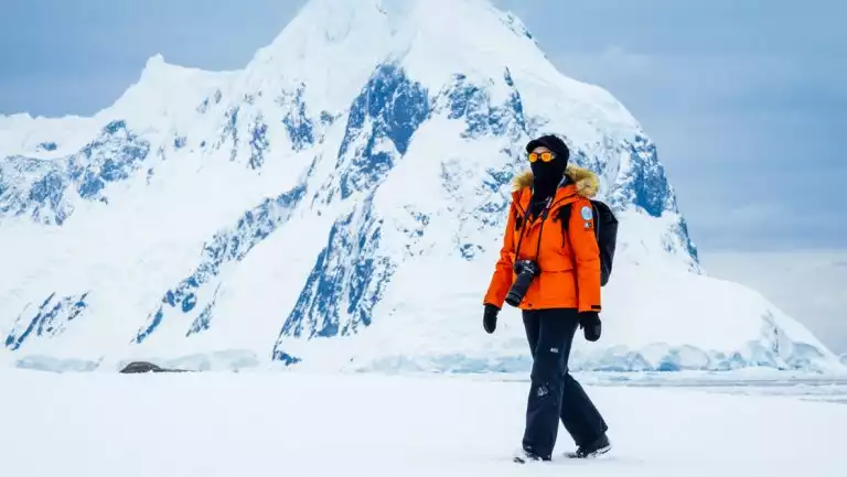 An Antarctic traveler in orange parka hikes over a snowfield during a photo expedition on Peterman Island, Antarctica.