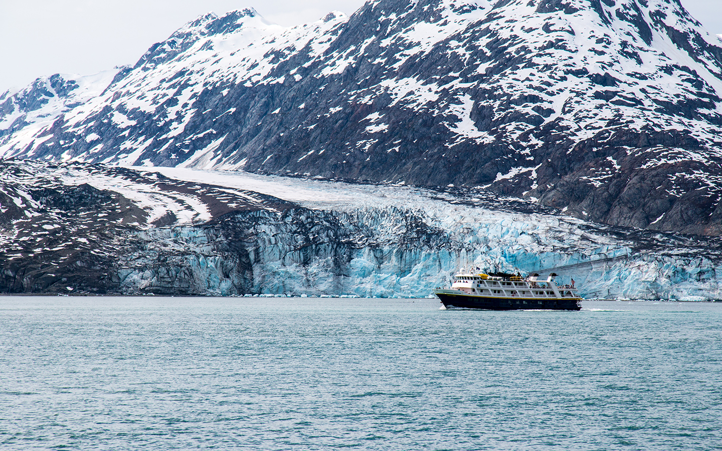 A small ship seen in front of a blue tidewater glacier in Alaska