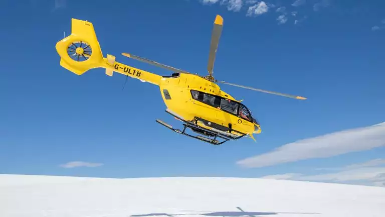 A bright yellow helicopter takes flight off the snow covered mountains