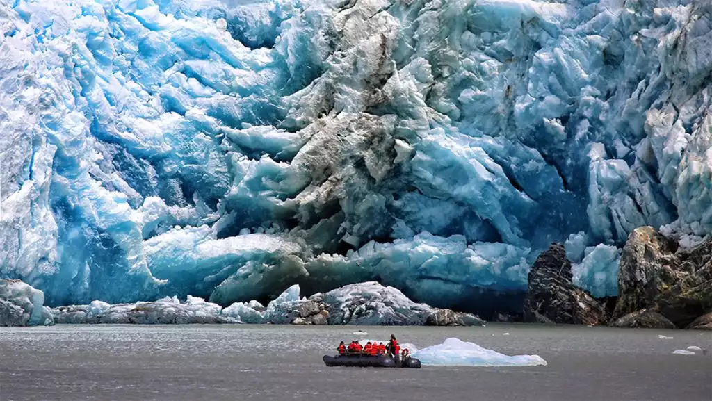 black inflatable skiff carrying group of guests navigates close to glacier in Alaska
