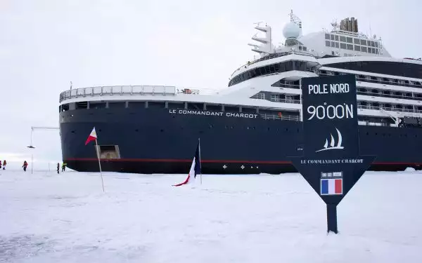 White and navy blue luxury ice breaker Le Commandant Charcot parked in ice at the North Pole with Blue arrow north pole sign