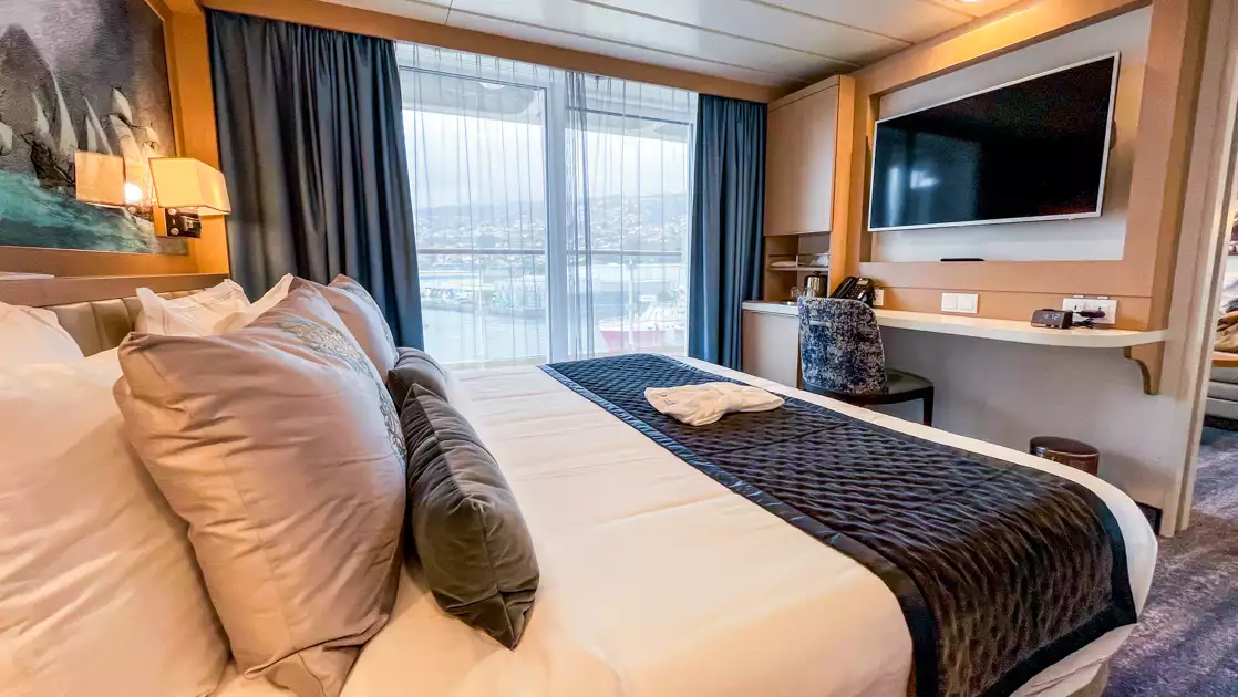Explorer suite bedroom on Ocean Explorer with double bed in white sheets by floor-to-ceiling windows & big balcony.