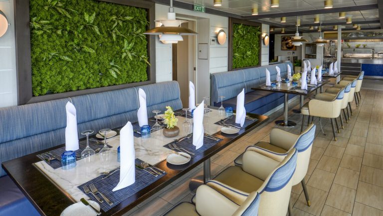 Restaurant on Ocean Explorer ship with living green wall art, bench & chair seats & long tables all in blue & cream decor.