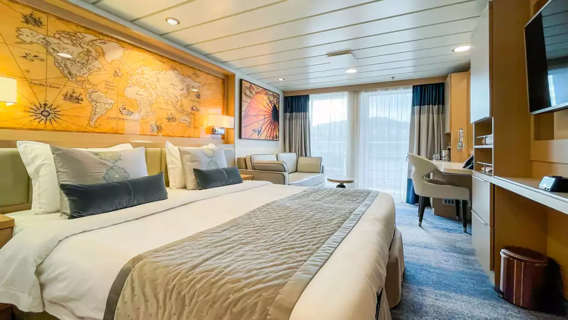 Deluxe Veranda Stateroom on Ocean Explorer ship with double bed in white sheets, desk, map headboard & balcony.