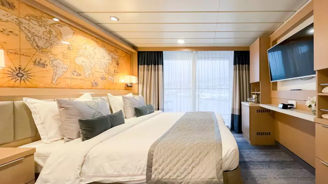 Deluxe Veranda forward Stateroom on Ocean Explorer ship with double bed in white sheets, desk, map headboard & balcony.