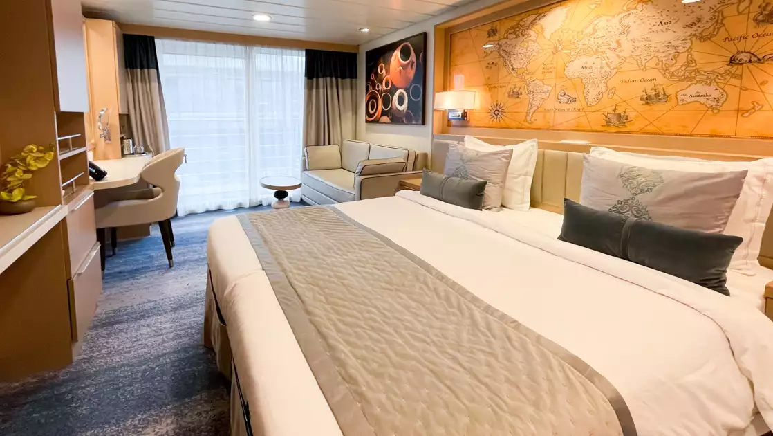 Deluxe Veranda Middle Stateroom on Ocean Explorer ship with double bed in white sheets, desk, map headboard & balcony.