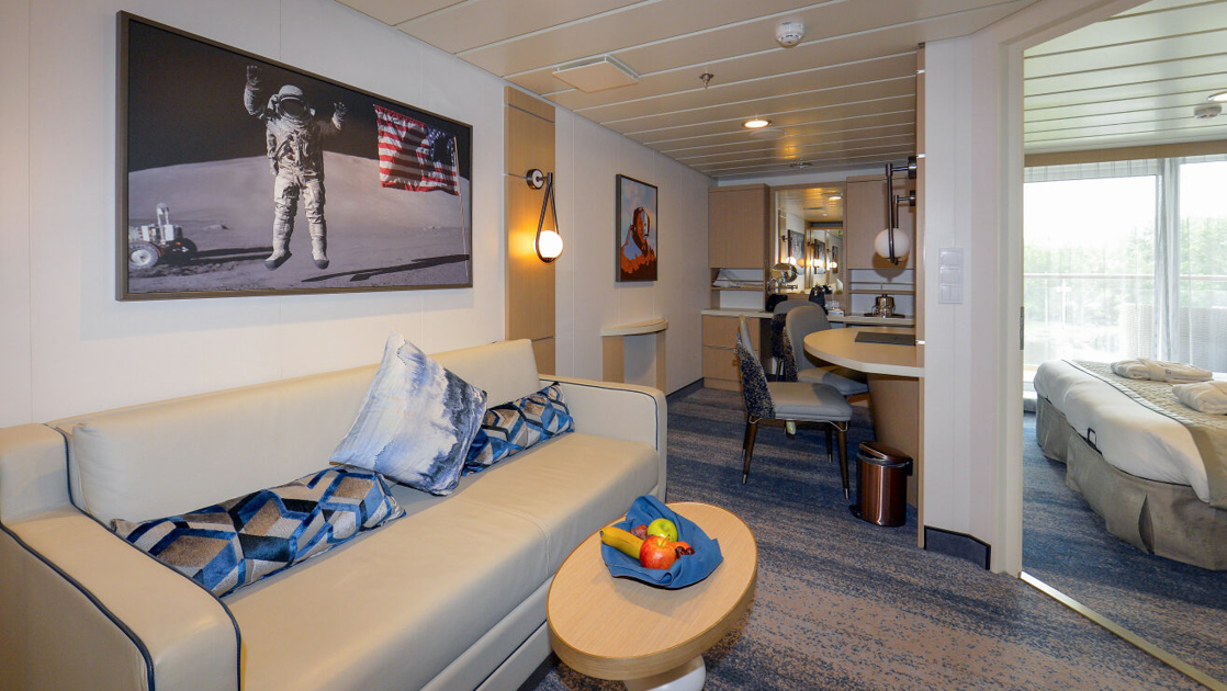 Junior Suite second room in blue, gray & beige on Ocean Explorer ship with modern couch, wood coffee table, desk & photo art.