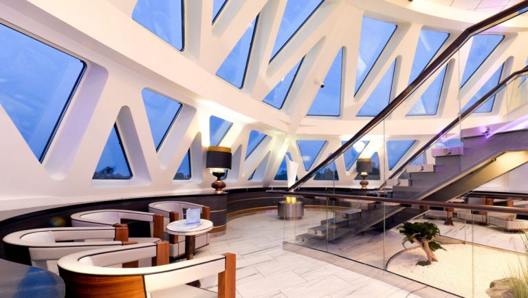 Glass atrium with triangular windows, white & wood captain's chairs, tile floor & large staircase on Ocean Explorer ship.