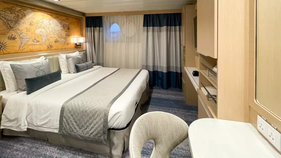 Studio Double cabin on Ocean Explorer ship with double bed in white sheets, desk, map headboard & 2 portholes.