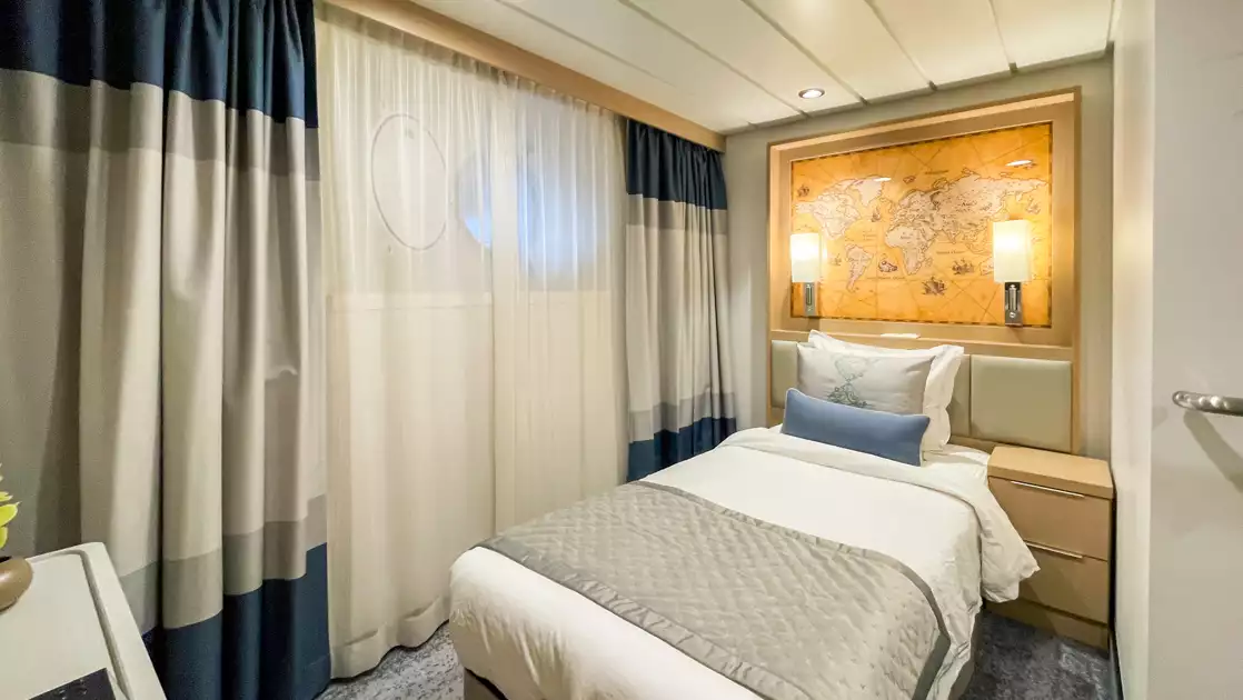 Studio Single cabin on Ocean Explorer ship with twin bed in white sheets, wood bedside table, map headboard & 2 portholes.