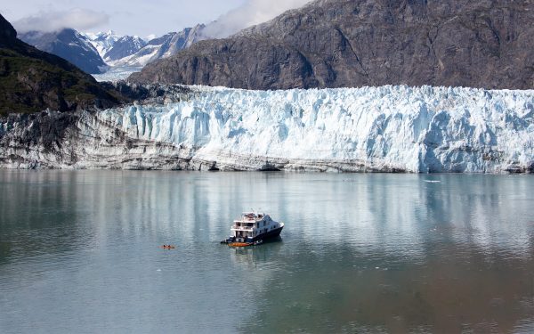A ship is anchored near a glacier as adventurers utilize kayaks to explore the waters nearby and get up close