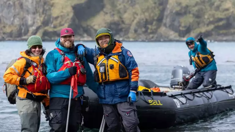adventurists in outdoor gear are possed for a picture getting off a small skiff off the water