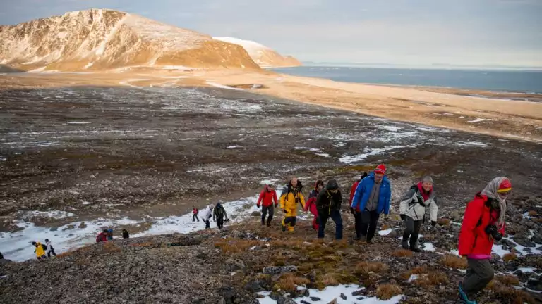 Hikers exploring the arctic landcapes dressed in cold weather gear as the sun sets behind them