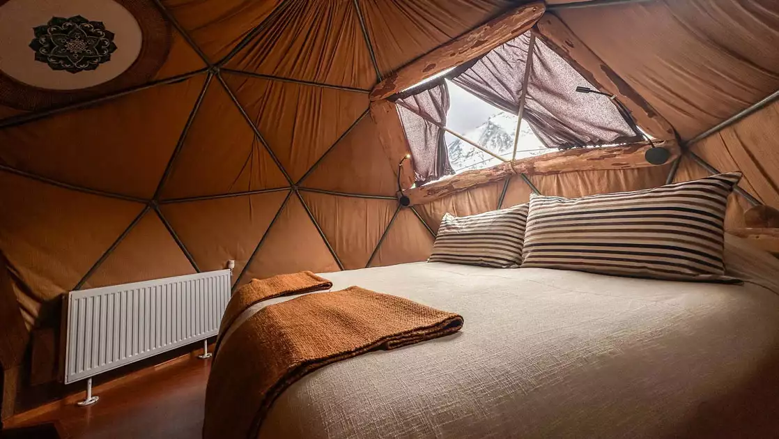 Standard Dome at EcoCamp with double bed, view window & white radiator, with earth tone decor.