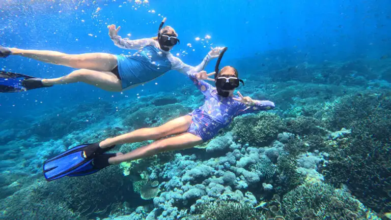 Mother & daughter snorkel in blue sea above colorful corals on a Jewels of Raja Ampat Indonesia sailing cruise.